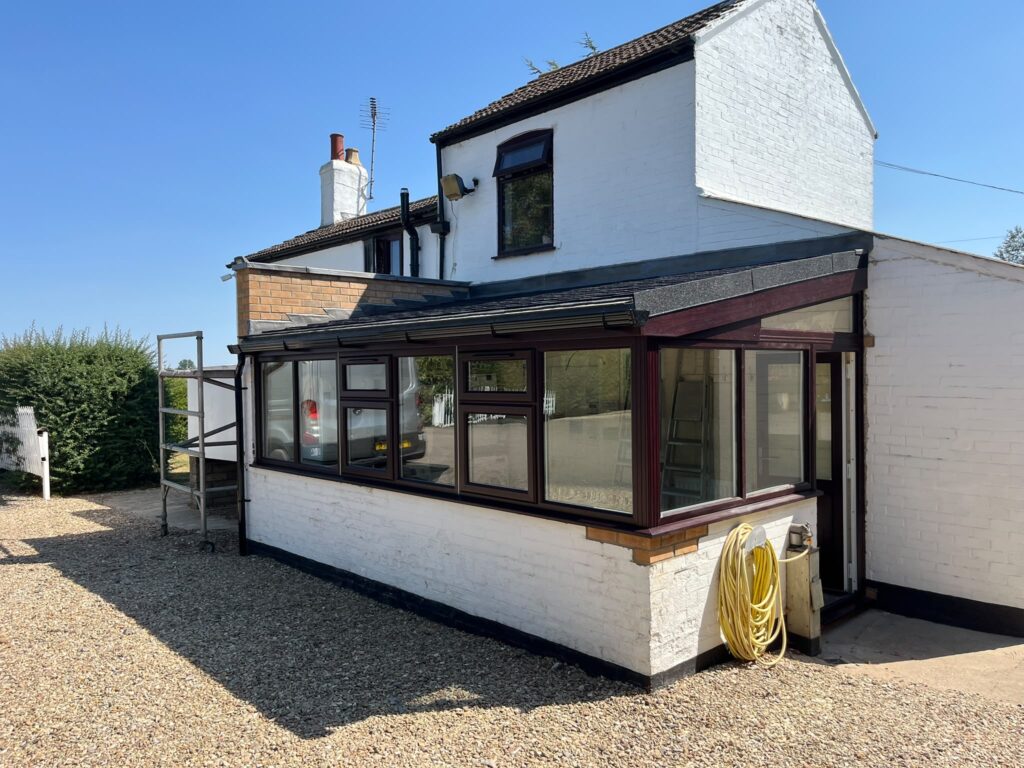 Exterior view of a house with a dark-framed conservatory and tiled replacement roof.